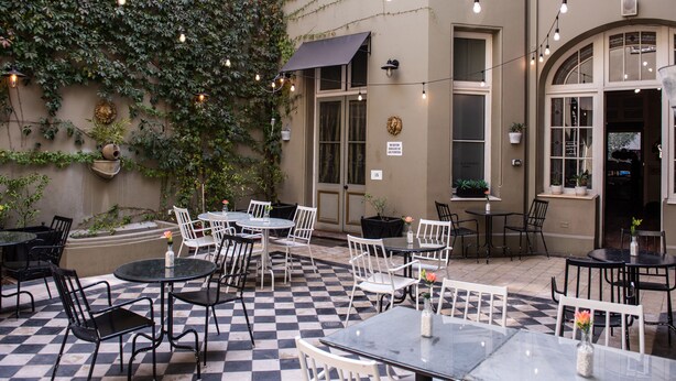 Un patio al aire libre con mesas, sillas, piso a cuadros y luces colgantes.