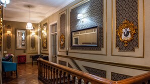 Un amplio pasillo con decoraciones elaboradas en las paredes, una escalera de madera y una silla azul.