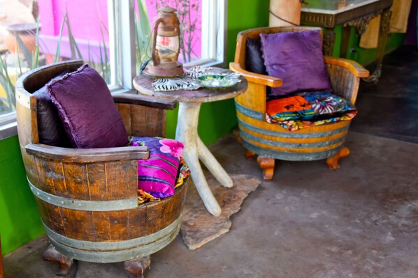 Two rustic wooden chairs with cushions, a small table with a lantern, and a window with a view of pink foliage.