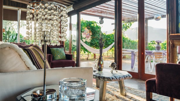 Una sala de estar acogedora con una lámpara de araña grande, un posavasos de vidrio y vistas a un jardín a través de amplios ventanales.