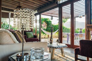 A cozy living room with a large chandelier, a glass ashtray, and a view of a garden through large windows.