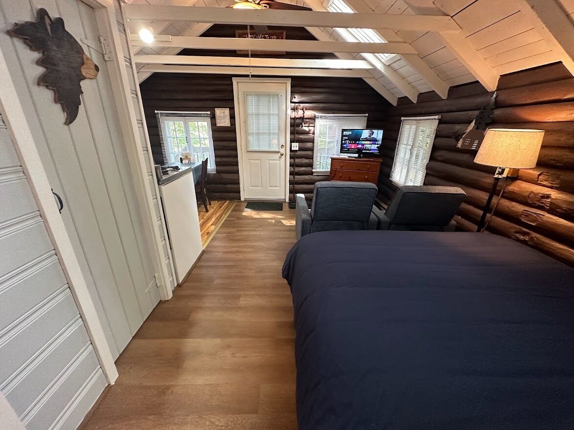Interior de una cabaña de troncos con un dormitorio, una pequeña cocina y una sala de estar.