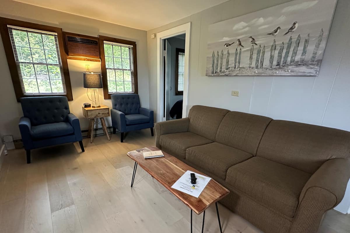 A living room with a brown sofa, two blue armchairs, a wooden coffee table with a notebook, and a lamp.