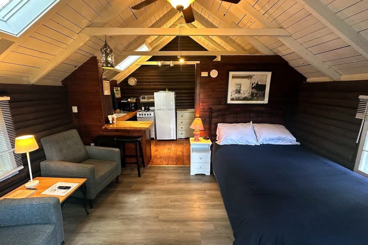 A cozy attic bedroom with a bed, a desk, and a kitchenette.