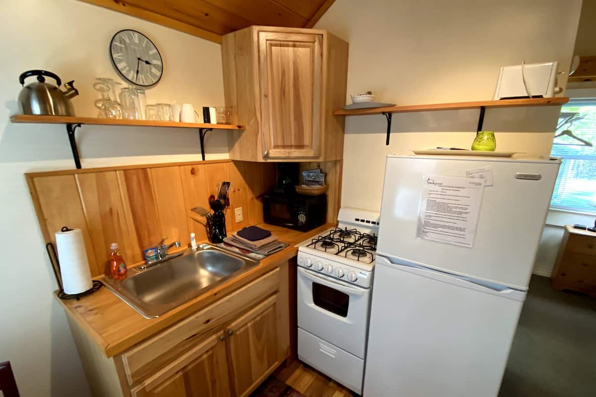A compact kitchen with wooden cabinets, a gas stove, a white refrigerator, and a clock on the wall.