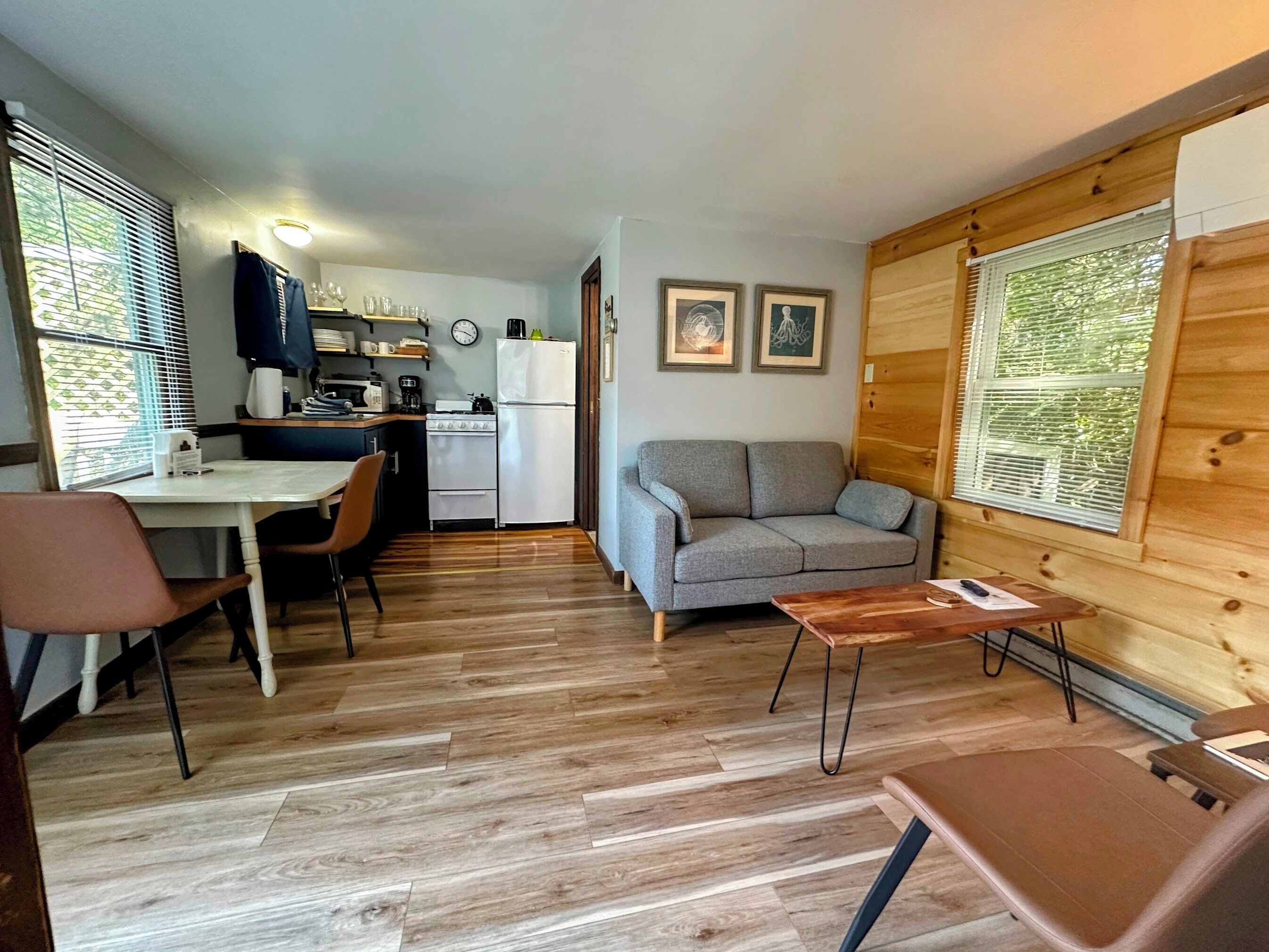 A compact living space with a kitchenette, a sofa, a dining table, and a wooden wall.