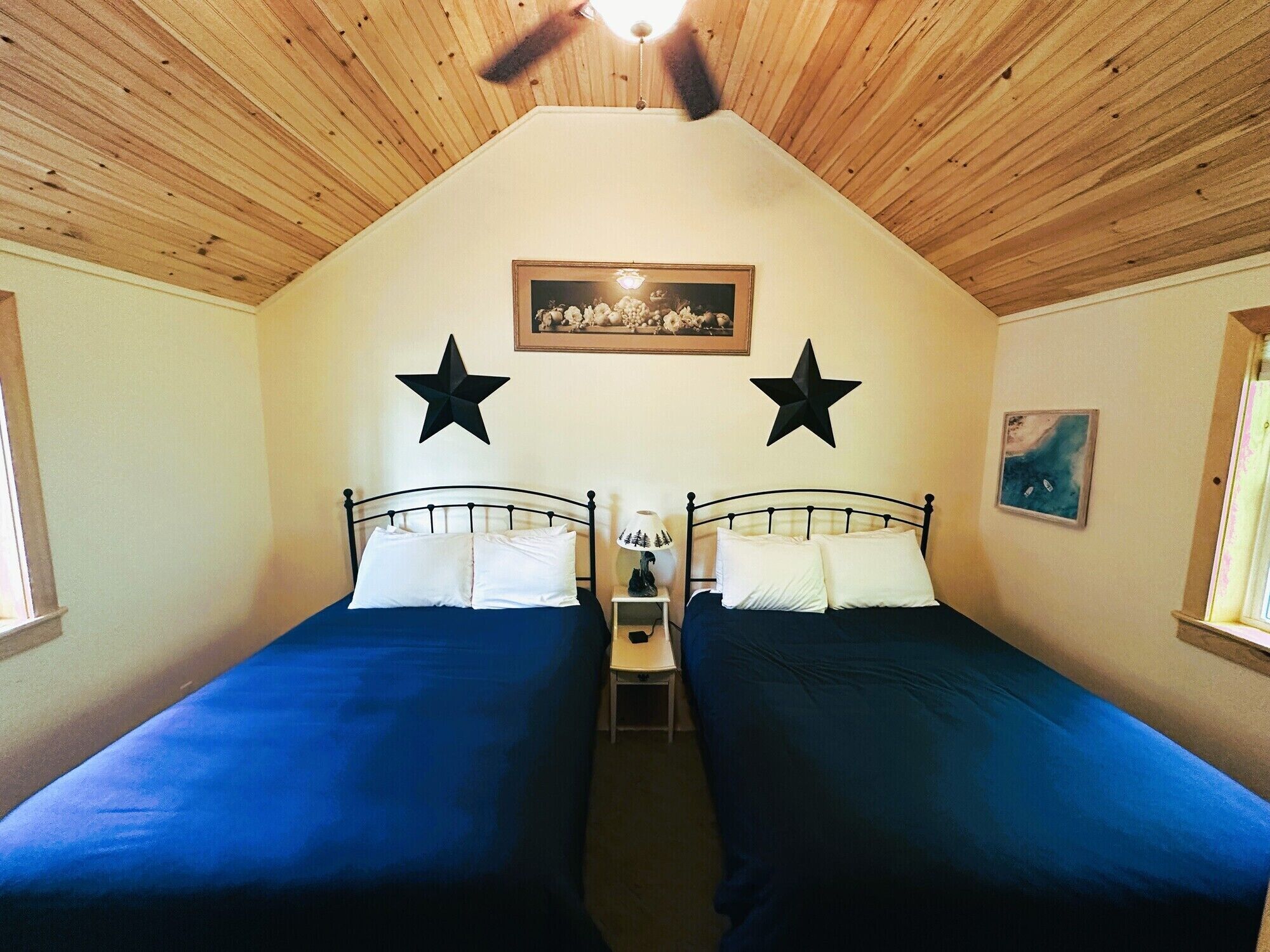 Una habitación con dos camas, un ventilador de techo, un cuadro enmarcado y dos estrellas en la pared.