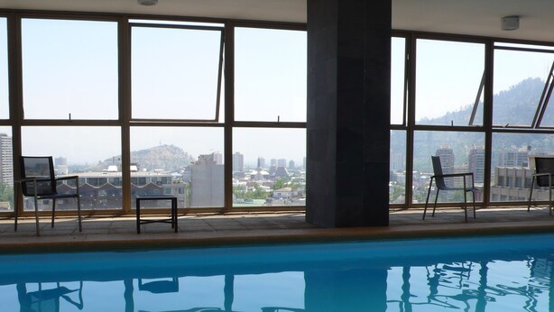 An indoor swimming pool with clear views of a cityscape through large windows. - Plaza Town Santiago (Santiago)