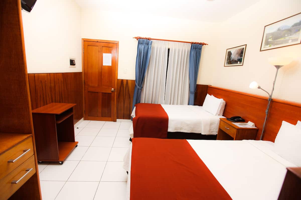 A hotel room with two beds, a desk, a wardrobe, a door, and a window with curtains.