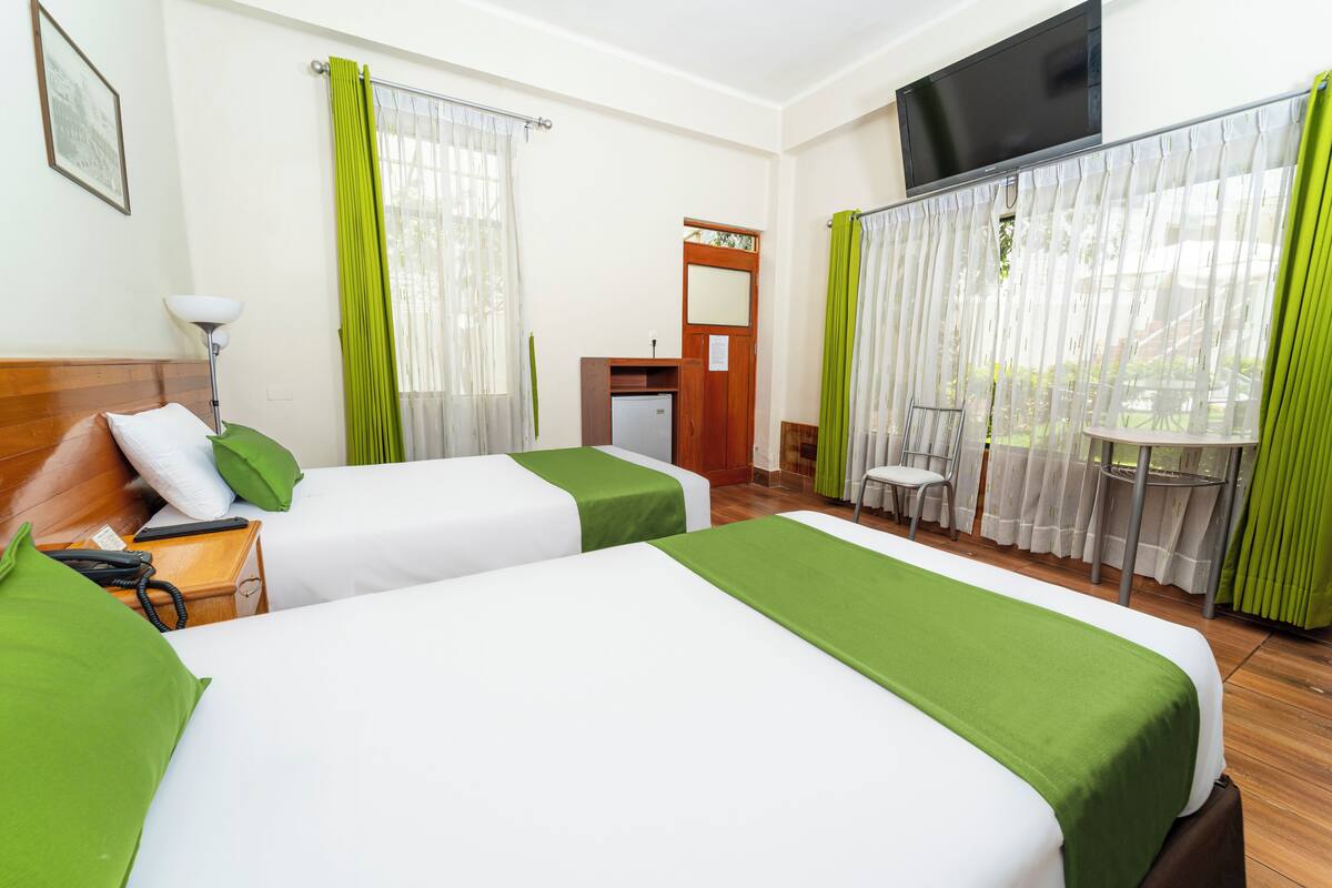 A hotel room with two beds, a desk with a telephone, a chair, a small table, and a TV on the wall.
