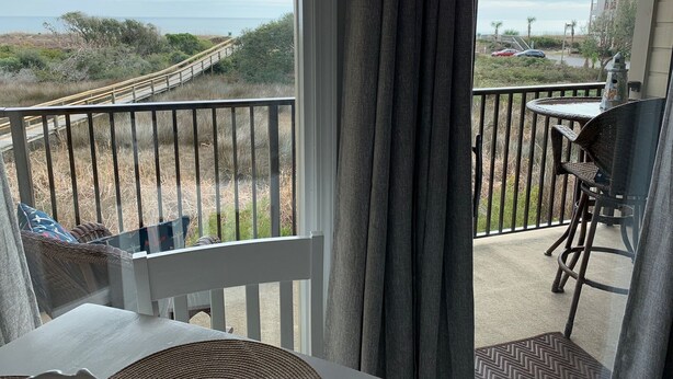 A balcony with a view of a beach and a wooden walkway.