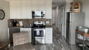 A modern kitchen with white cabinets, a stainless steel refrigerator, a microwave, a stove, and a ceiling fan.