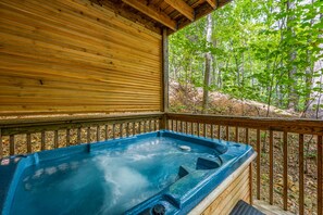 A wooden deck with a hot tub surrounded by a forest.