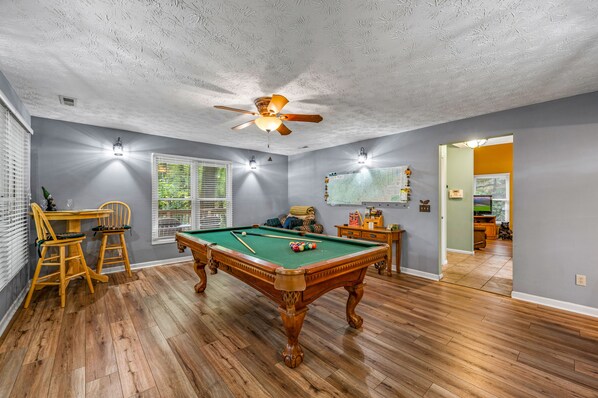 A pool table in a room with wooden flooring, a ceiling fan, and two wall-mounted lights.