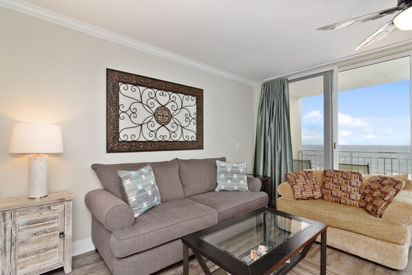 A living room with a grey sofa, a beige sofa, a glass coffee table, and a decorative wall piece.