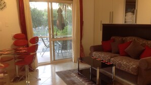 A living room with a sofa, red chairs, a glass table, and a view of the outdoors through a sliding door. - Stunning studio holiday apartment for 2/3 on resort, close to beach with 2 pools (Pizzo)