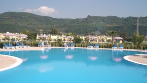 A swimming pool with lounge chairs and umbrellas, surrounded by buildings and hills. - Stunning studio holiday apartment for 2/3 on resort, close to beach with 2 pools (Pizzo)