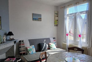 Ein Schlafzimmer mit einem Bett, einem Sessel, einem Tisch, einer Lampe, einem Heizkörper und einem Fenster mit Vorhängen.