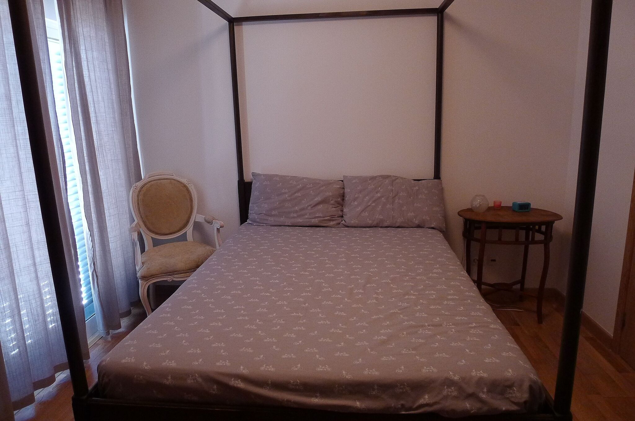 A bedroom with a four-poster bed, a chair, and a small table.