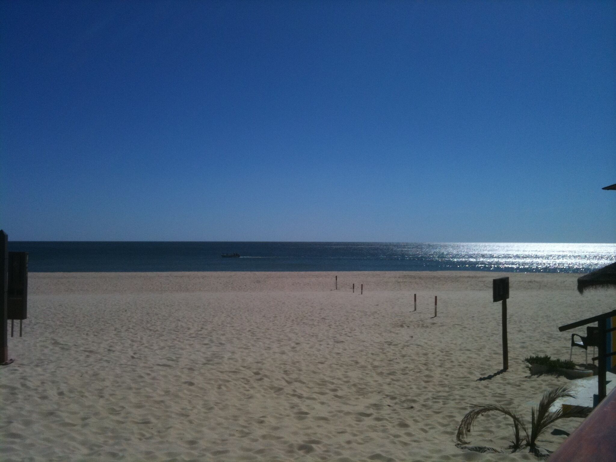 A beach with a clear sky, a boat on the water, and a sandy shore.