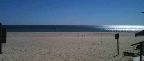 A beach with a clear sky, a boat on the water, and a sandy shore.