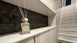 Ein modernes Badezimmer mit einem weißen Waschtisch, einer Wand in Dunkelholzoptik und einer Glasflasche Citrus Verbena auf dem Regal.