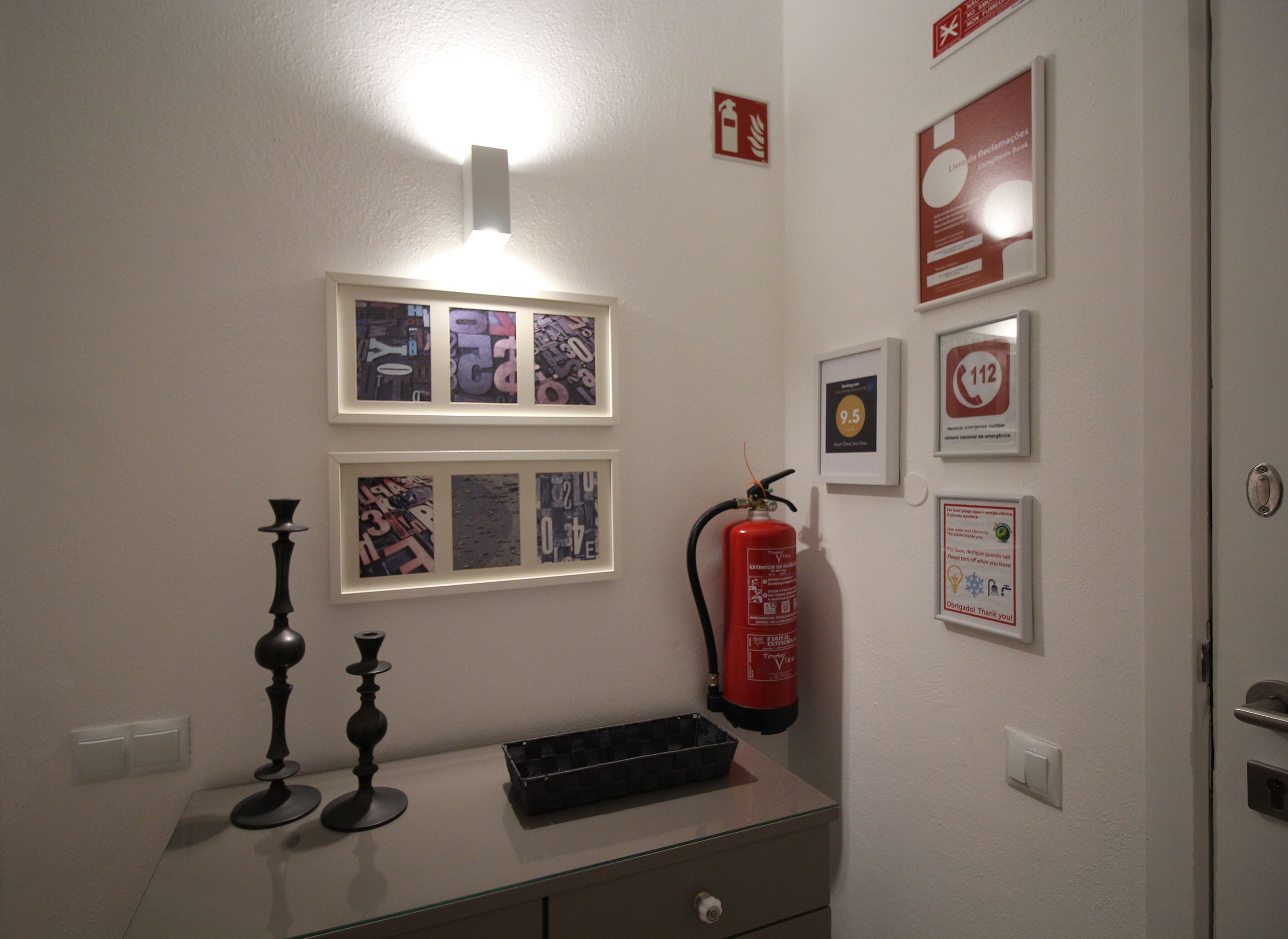En vägg med inramade bilder, en brandsläckare och telefonnummer till kontaktpersoner i nödsituationer.