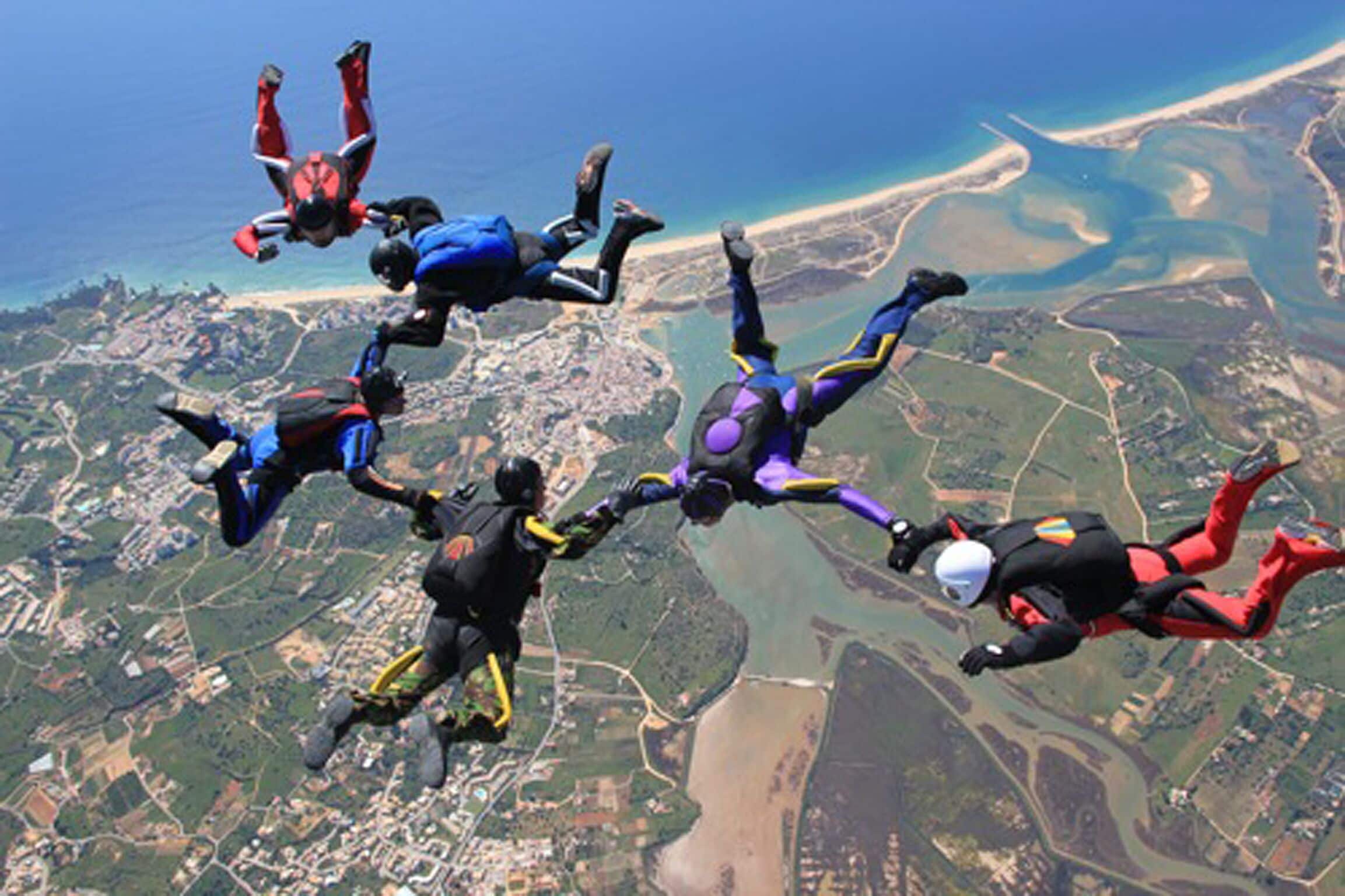 A group of skydivers in mid-air with a coastal landscape below.