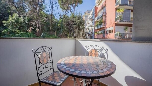 A balcony with a round table and two chairs, overlooking a residential area with trees and buildings.