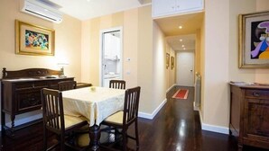A dining area with a table and chairs, a kitchen visible through an open door, and a hallway leading to another room.
