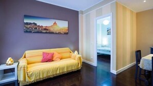 A living room with a sofa, a painting of a cityscape, and a dining area with a table and chairs.