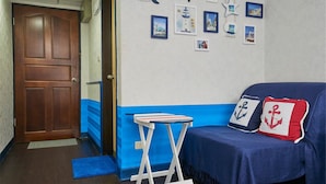 Une pièce avec une porte en bois, un mur bleu et blanc, un canapé bleu agrémenté de coussins à motifs nautiques et une petite table.