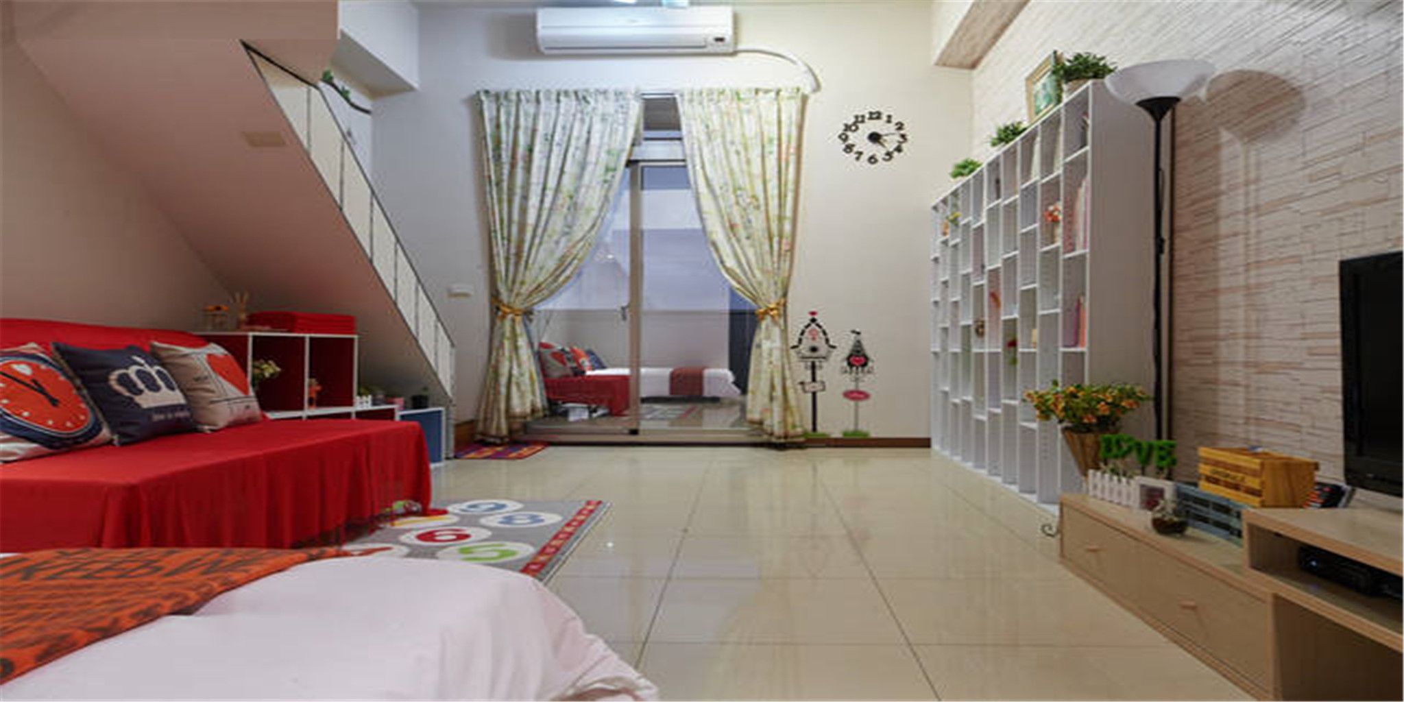 Quarto com sofá vermelho, televisão, estante de livros e escada que dá para outro cômodo.