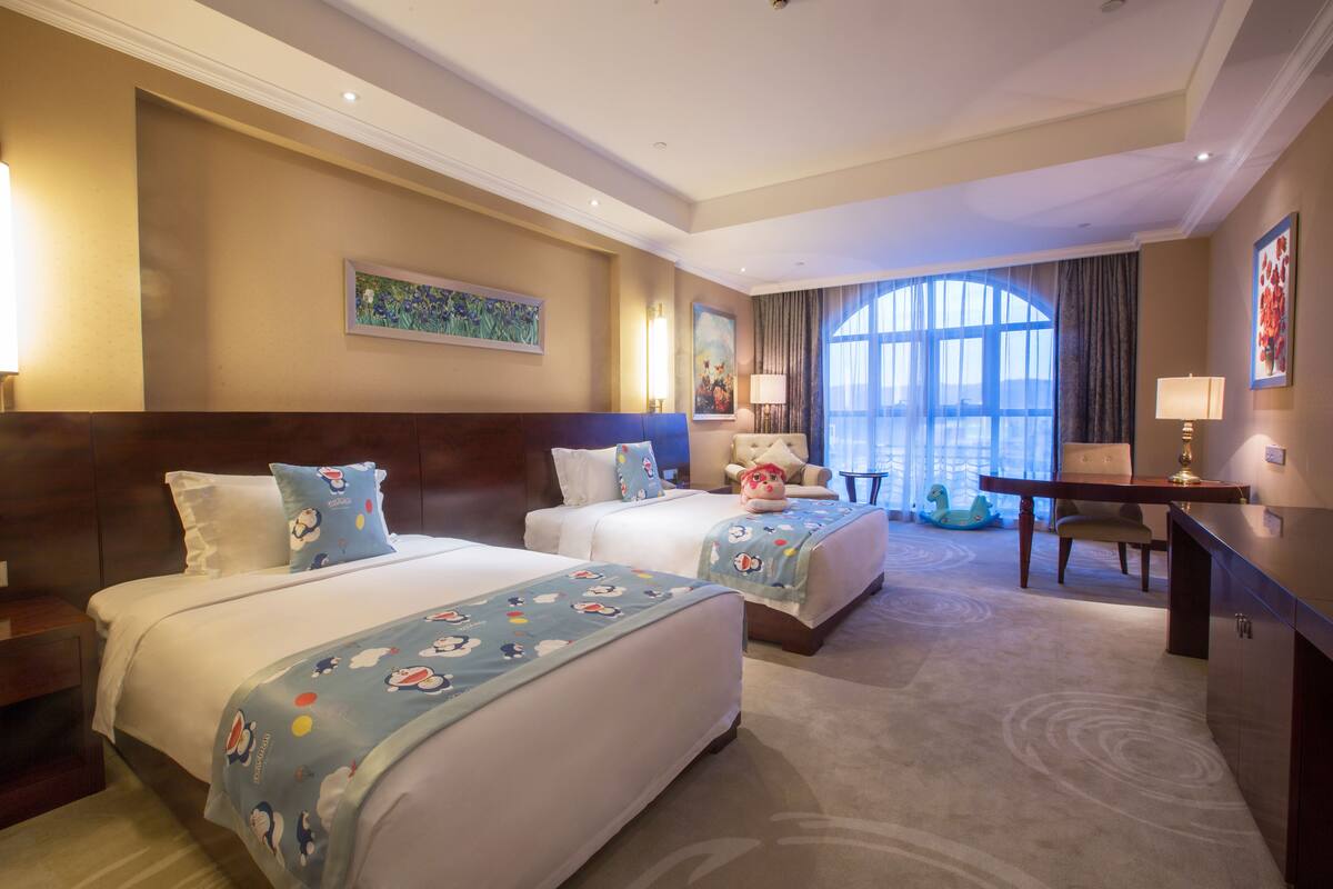 Ein Hotelzimmer mit zwei Betten, einem Schreibtisch und einem großen Fenster.