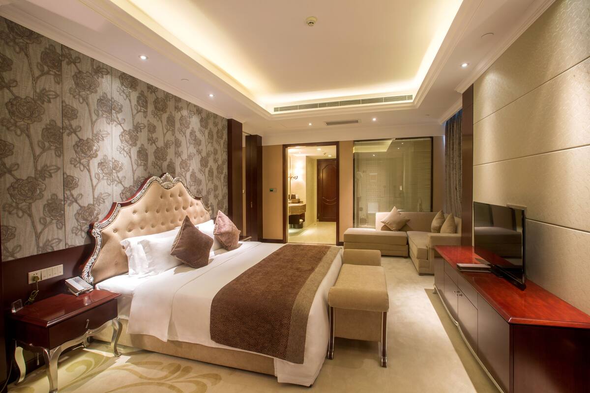 Ein Hotelzimmer mit einem großen Bett, einem Fernseher, einem Schreibtisch und einem durch eine offene Tür einsehbaren Badezimmer.