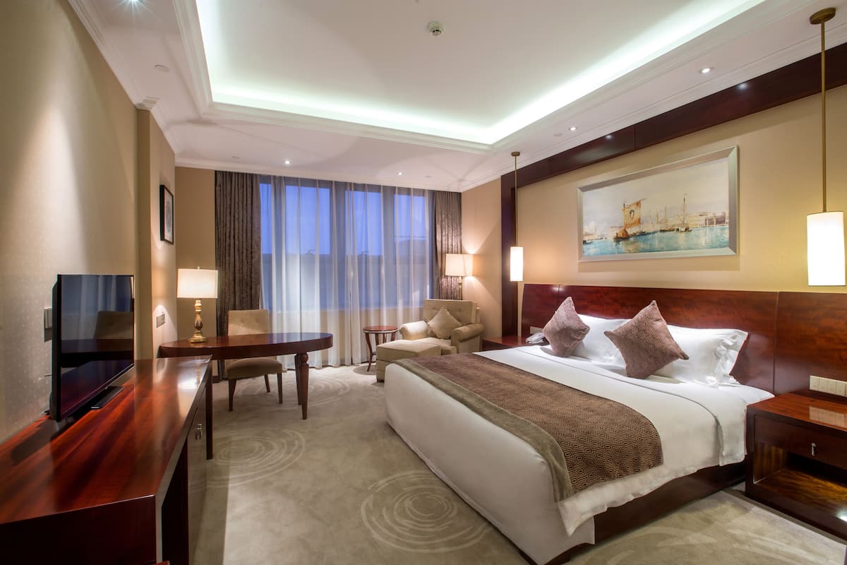 Ein Hotelzimmer mit einem großen Bett, einem Schreibtisch, einem Sessel, einem Fernseher und einem Bild an der Wand.