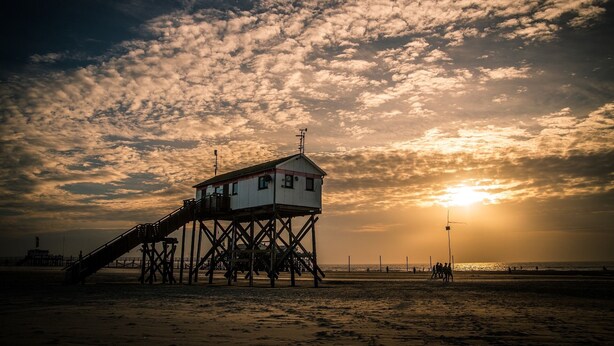 Un muelle de playa con una torre de salvavidas, una escalera y el océano al fondo durante la puesta de sol.