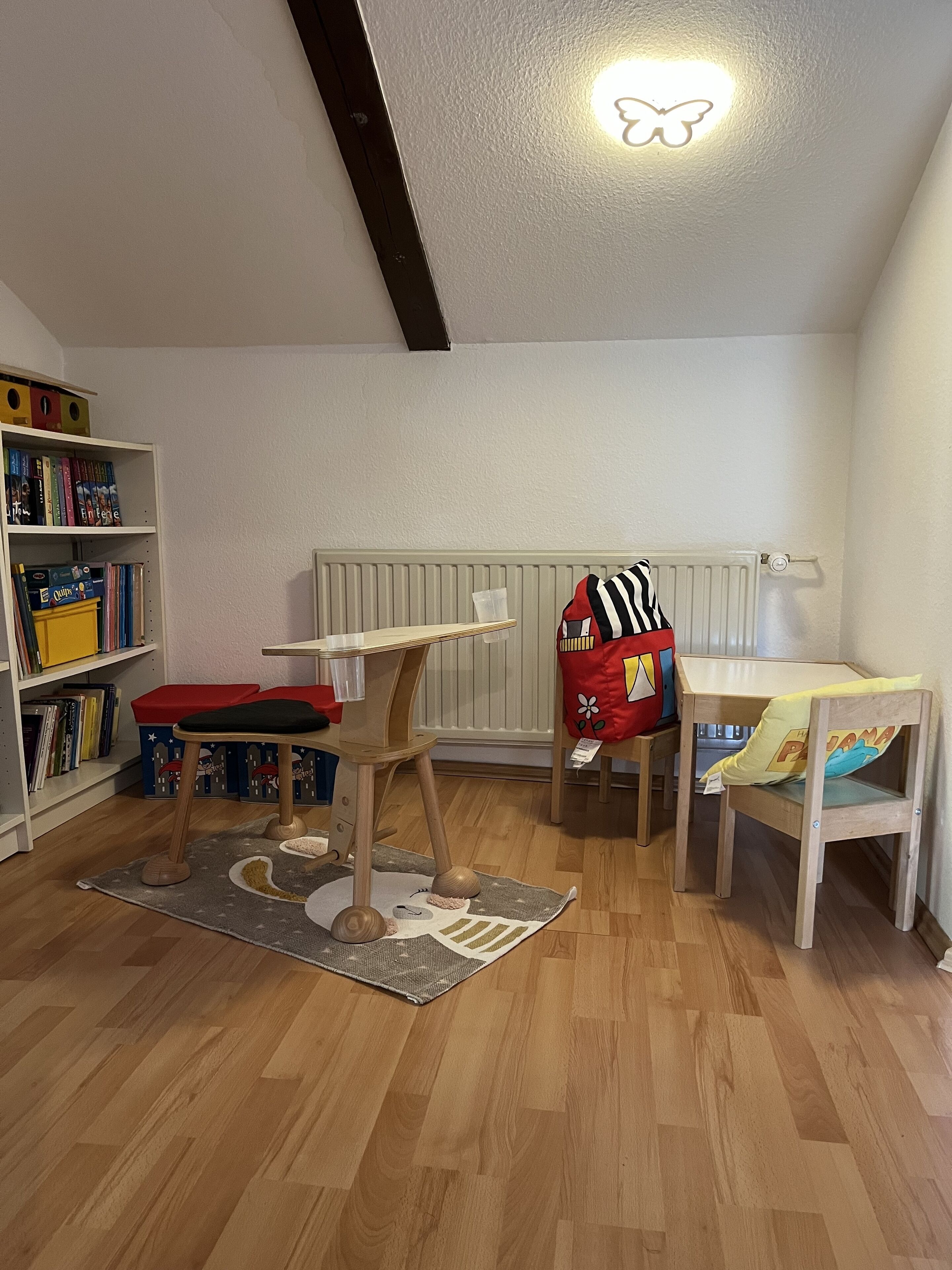 A child's playroom with a wooden floor, a bookshelf, a play table, and a cat tree.