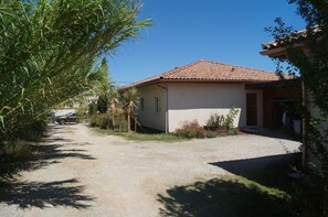 A single-story house with a tiled roof, a gravel driveway, and a small garden area with plants and a tree.