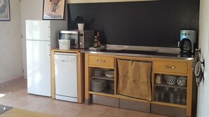Een kleine keuken met een magnetron, broodrooster en koffiezetapparaat op het aanrecht. Daaronder zijn kastjes met servies en glazen.