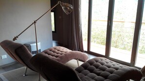 Une chambre moderne équipée d’un fauteuil inclinable, d’un lampadaire et d’une grande fenêtre donnant sur un paysage verdoyant.