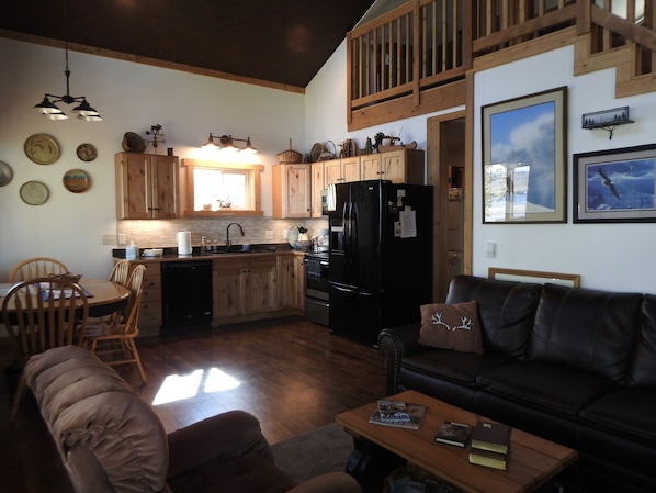 Una sala acogedora con sofá y una mesa de centro, una cocina con armarios de madera y un refrigerador negro, y un comedor con sillas y una mesa.