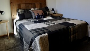 Una camera da letto con una testiera in legno, una coperta trapuntata, numerosi cuscini, una lampada da comodino e un piccolo comodino in legno.