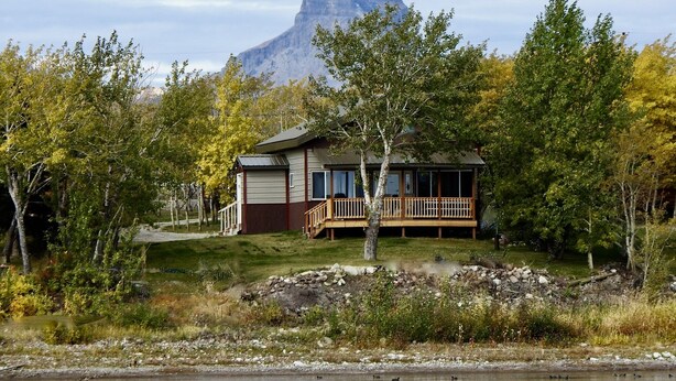 Une cabane dotée d’une terrasse, entourée d’arbres et avec une montagne en toile de fond.
