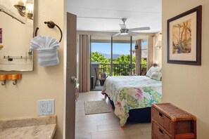 A hotel room with a bed, a ceiling fan, a view of the outdoors, a bathroom with a towel rack, and a painting on the wall. - 30% Disc Last Min, 48 Hr Cancel, Partial Ocean Vw,  A/C, 3 min to Beach (Kihei)