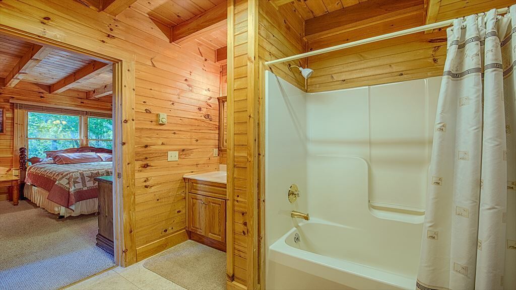 Een houten chalet met een slaapkamer, een badkamer met een badkuip, en een kleine kitchenette.