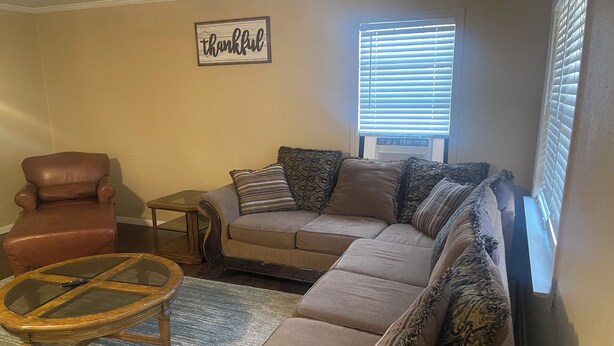 A living room with a brown leather armchair, a beige sectional sofa with patterned cushions, a glass coffee table, and a small wooden side table. - Spacious 4 Bedroom Vacation Home   6 Beds (Garland)