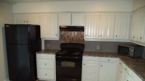 A kitchen with white cabinets, a black refrigerator, a stove, and a microwave. - Spacious 4 Bedroom Vacation Home   6 Beds (Garland)