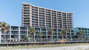 Et hotel med flere etager, altaner, udsigt til stranden og palmer.