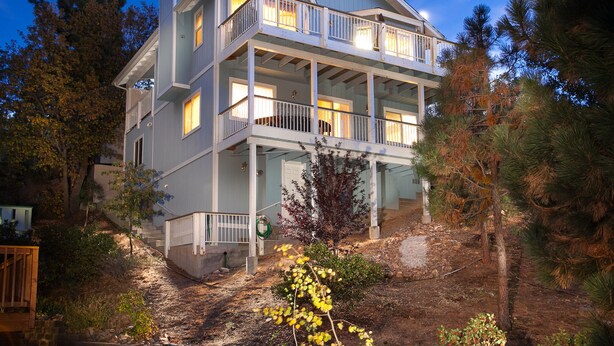 A two-story house with a balcony on the second floor, surrounded by trees.